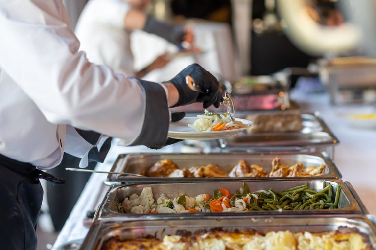 In a spacious and bright event hall, catering staff is actively serving a gourmet buffet